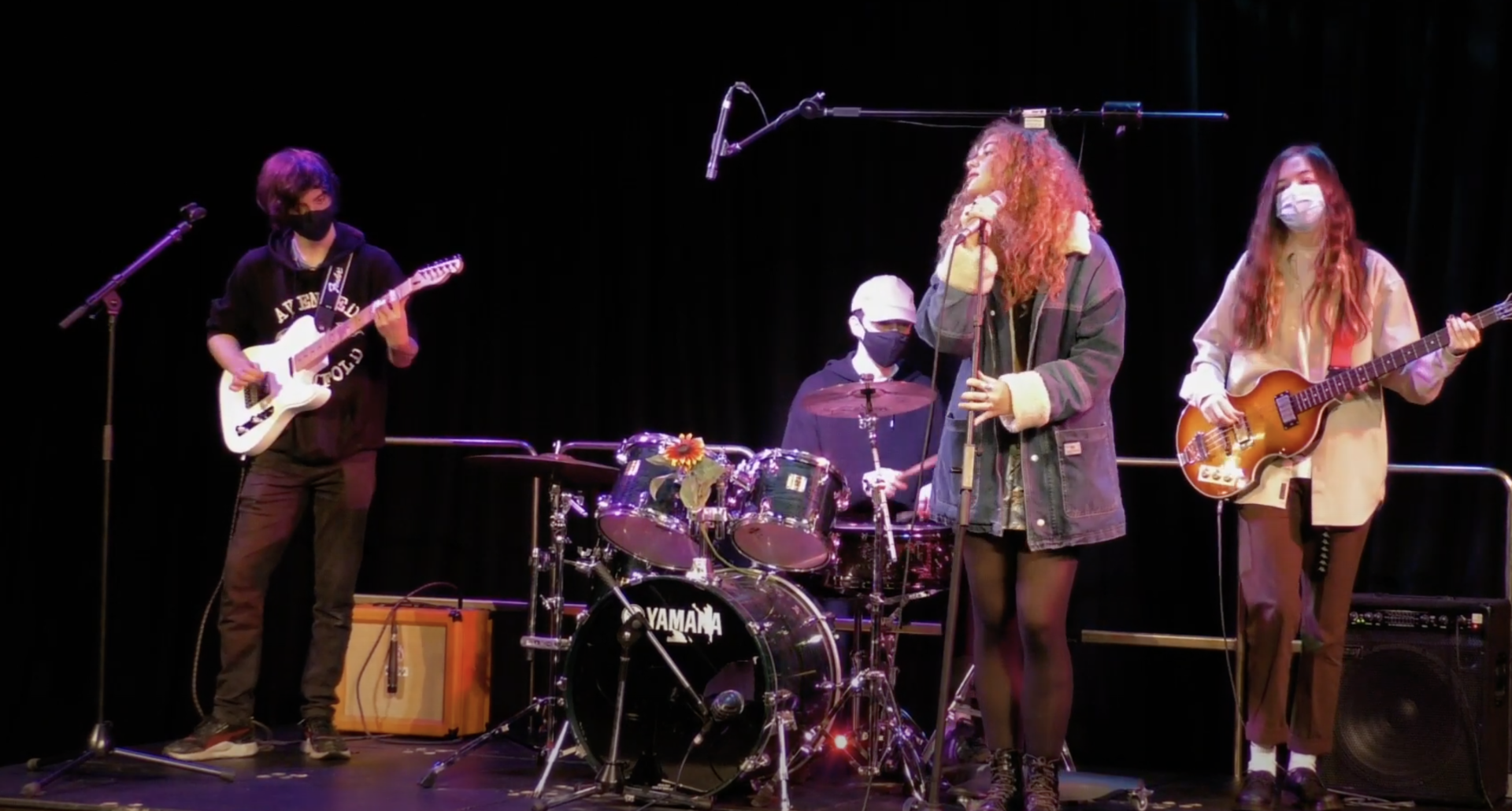 A group of people wearing face masks are playing instruments on a stage.
