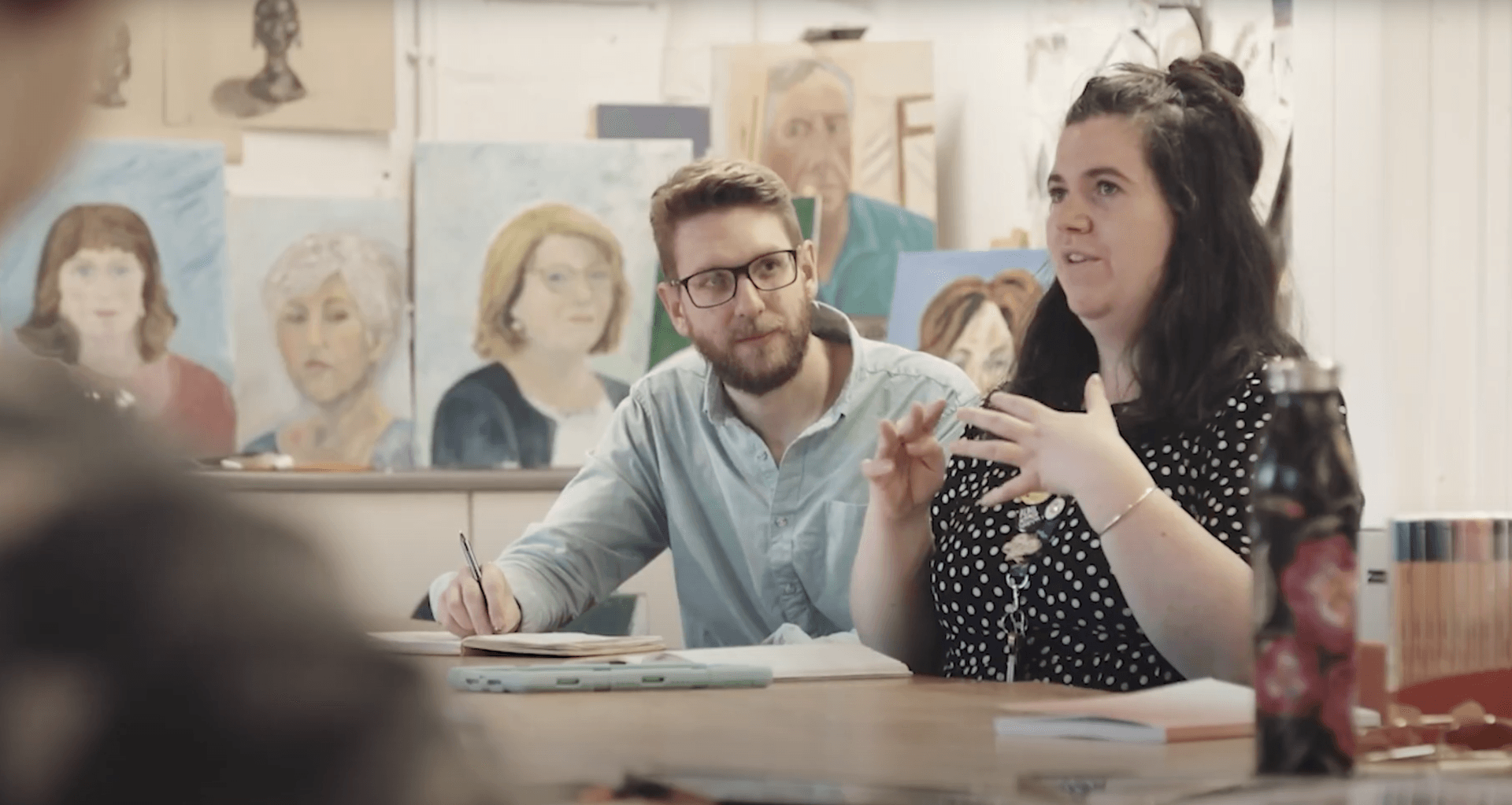 A man and a woman are sitting at a table in a classroom.