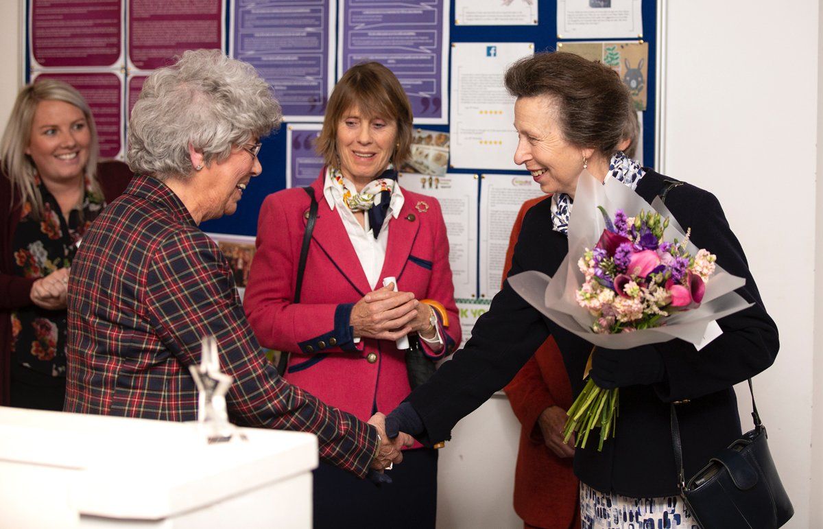 A woman is shaking hands with another woman while holding a bouquet of flowers.