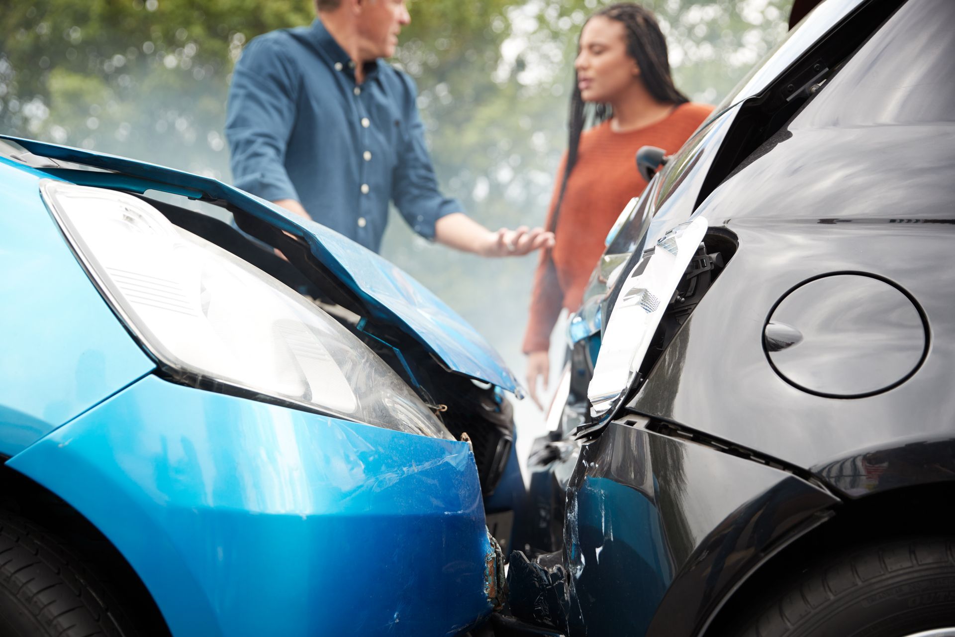 Two cars damaged in a collision; a man and woman stand nearby, looking concerned.