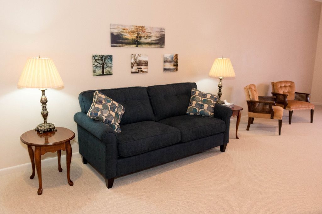 Living room with blue sofa, two lamps on side tables, two chairs, and art on the wall.