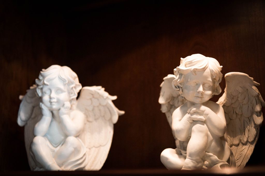 Two white cherub statues with wings on a dark background.