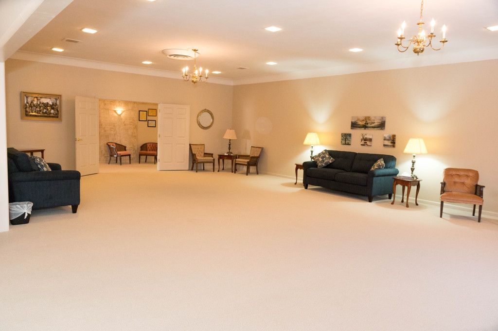 Spacious room with tan carpet and walls, couches, chairs, and two chandeliers.
