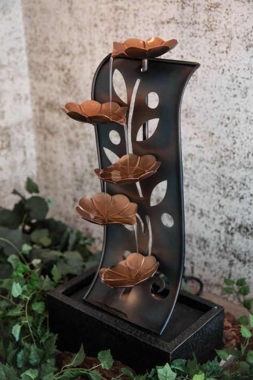 Water fountain with copper-colored leaf-shaped bowls, black metal frame, and water cascading down.