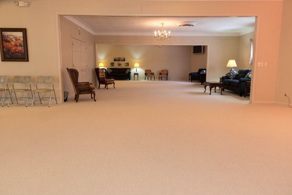 A large, empty room with beige carpet, seating areas, and a chandelier, possibly a funeral home.