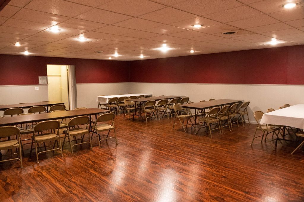 A brightly lit community hall with long tables and folding chairs set for a gathering.