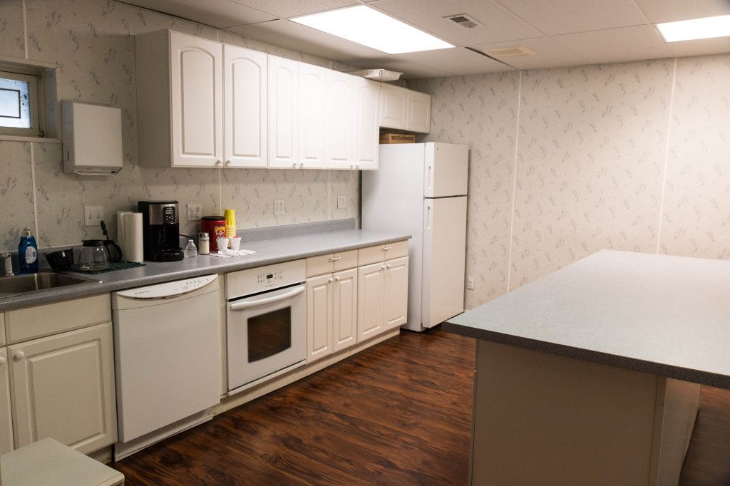 A small kitchen with white cabinets, appliances, and a counter. There's a white island in the foreground.