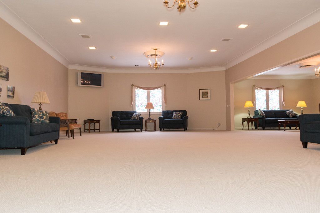 Spacious room with carpet, couches, lamps, and a small television. Beige walls and recessed lighting.