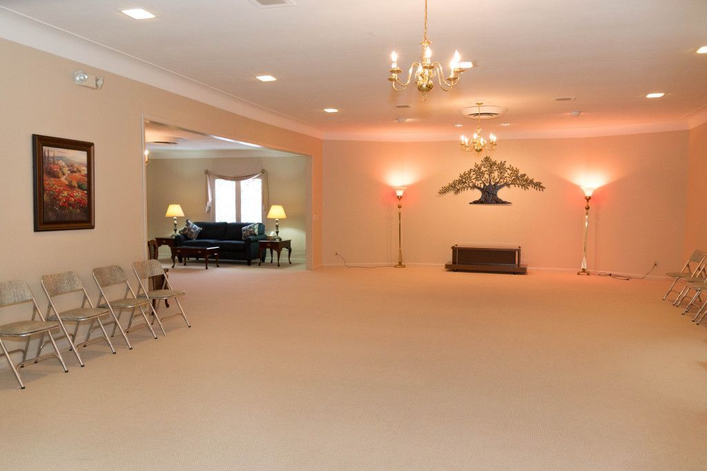 Empty funeral home viewing room with light beige carpet, neutral walls, and formal decor.