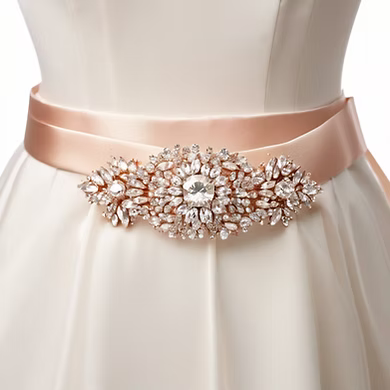 A woman is wearing a white dress with a rose gold belt with rhinestones.