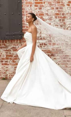 A woman in a wedding dress and veil is standing in front of a brick wall.