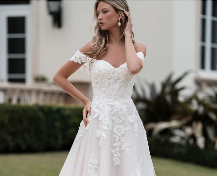 A woman in a white wedding dress is standing in front of a white building.