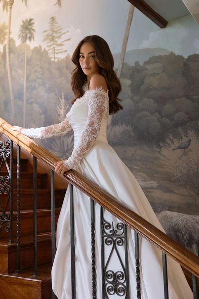 A woman in a wedding dress is standing next to a couch in front of a window.