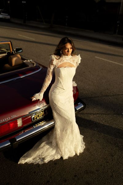 A woman in a wedding dress is standing next to a couch in front of a window.