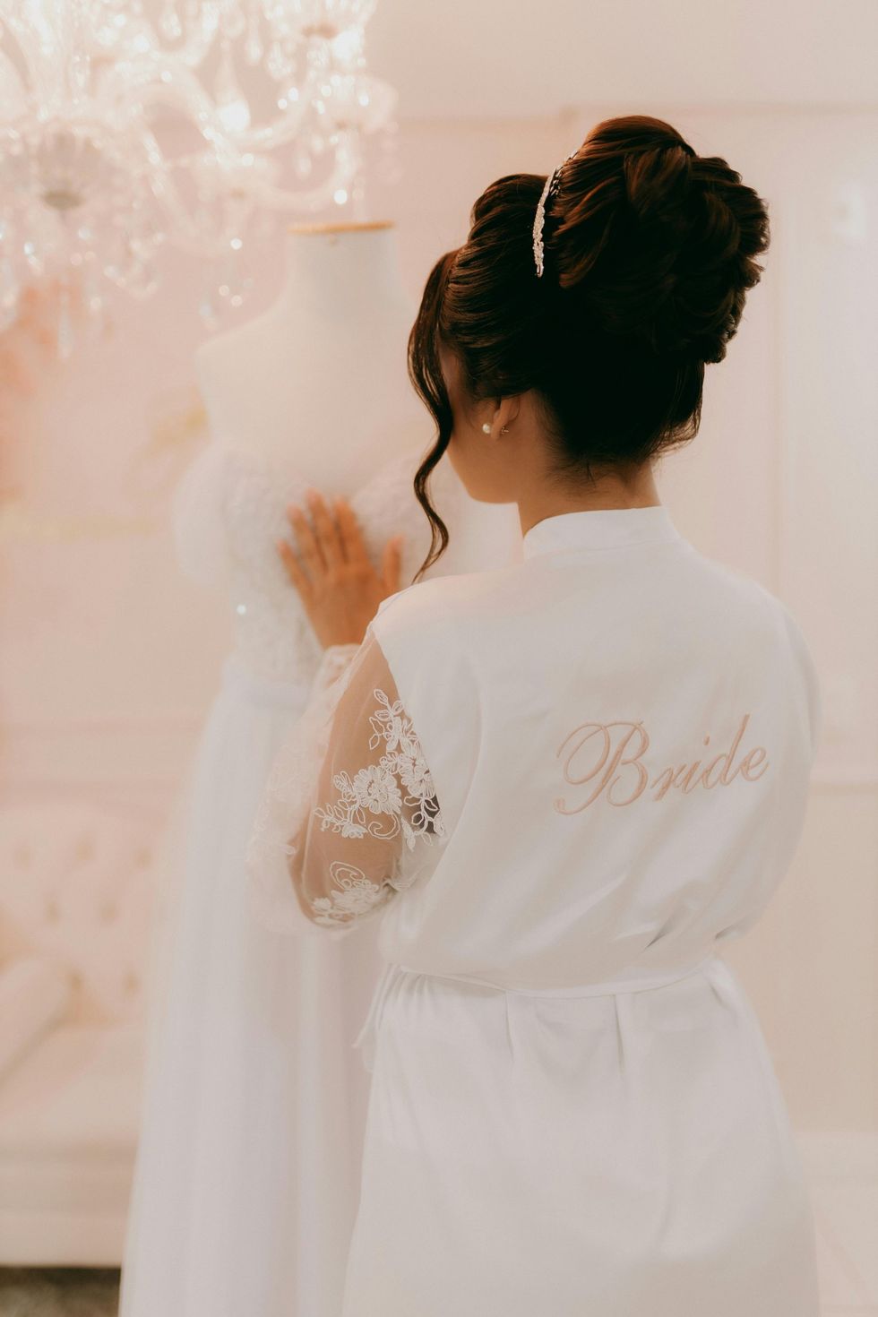 The bride is wearing a white robe and looking at her wedding dress.