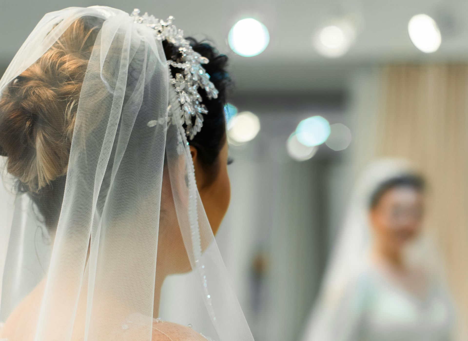 The bride is wearing a veil and looking at herself in the mirror.