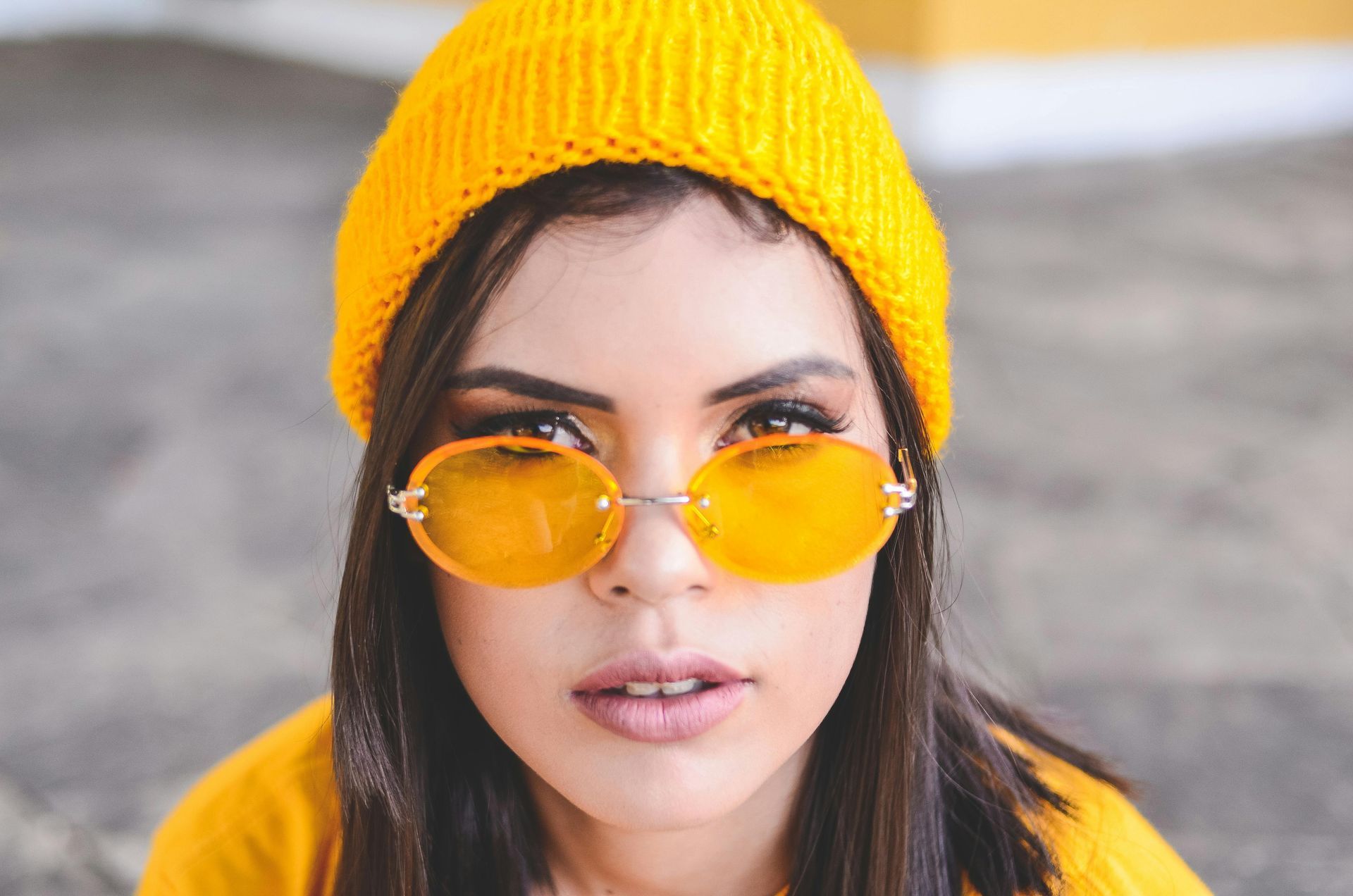 Woman wearing yellow beanie and sunglasses, looking at the camera.
