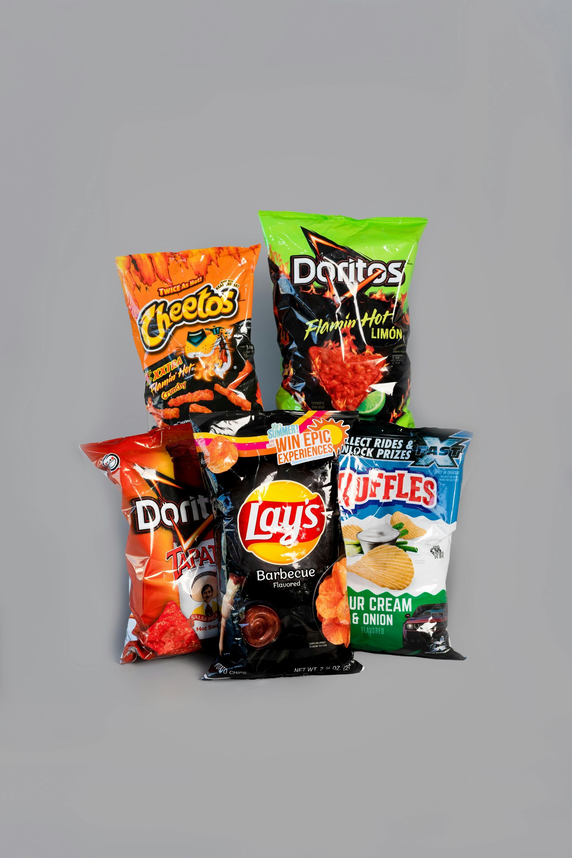 Five bags of chips: Cheetos, Doritos, Lays, and Ruffles on a gray background.