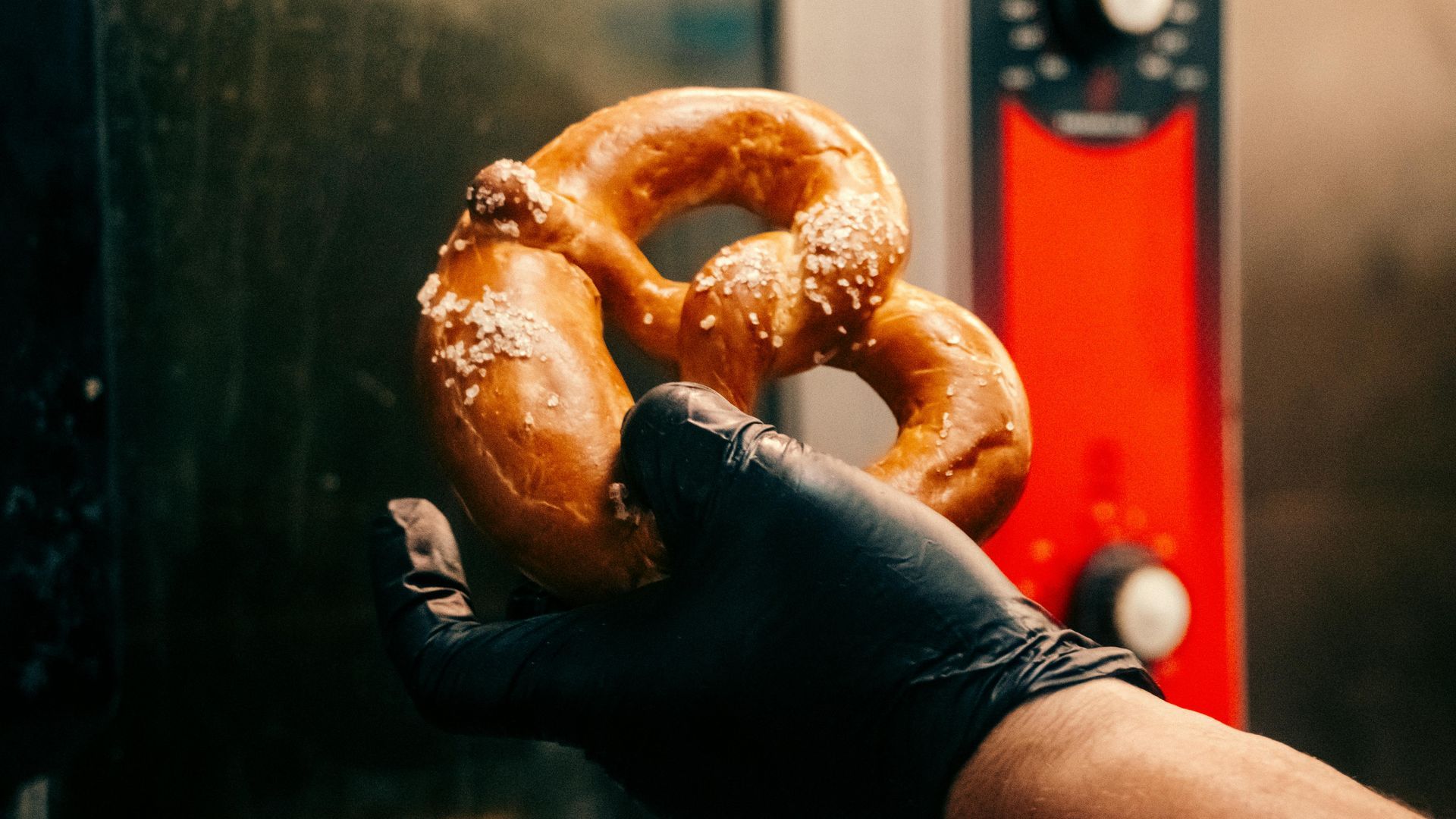 Pretzels and pretzel bread rolls on a black wire rack, against a gray background.