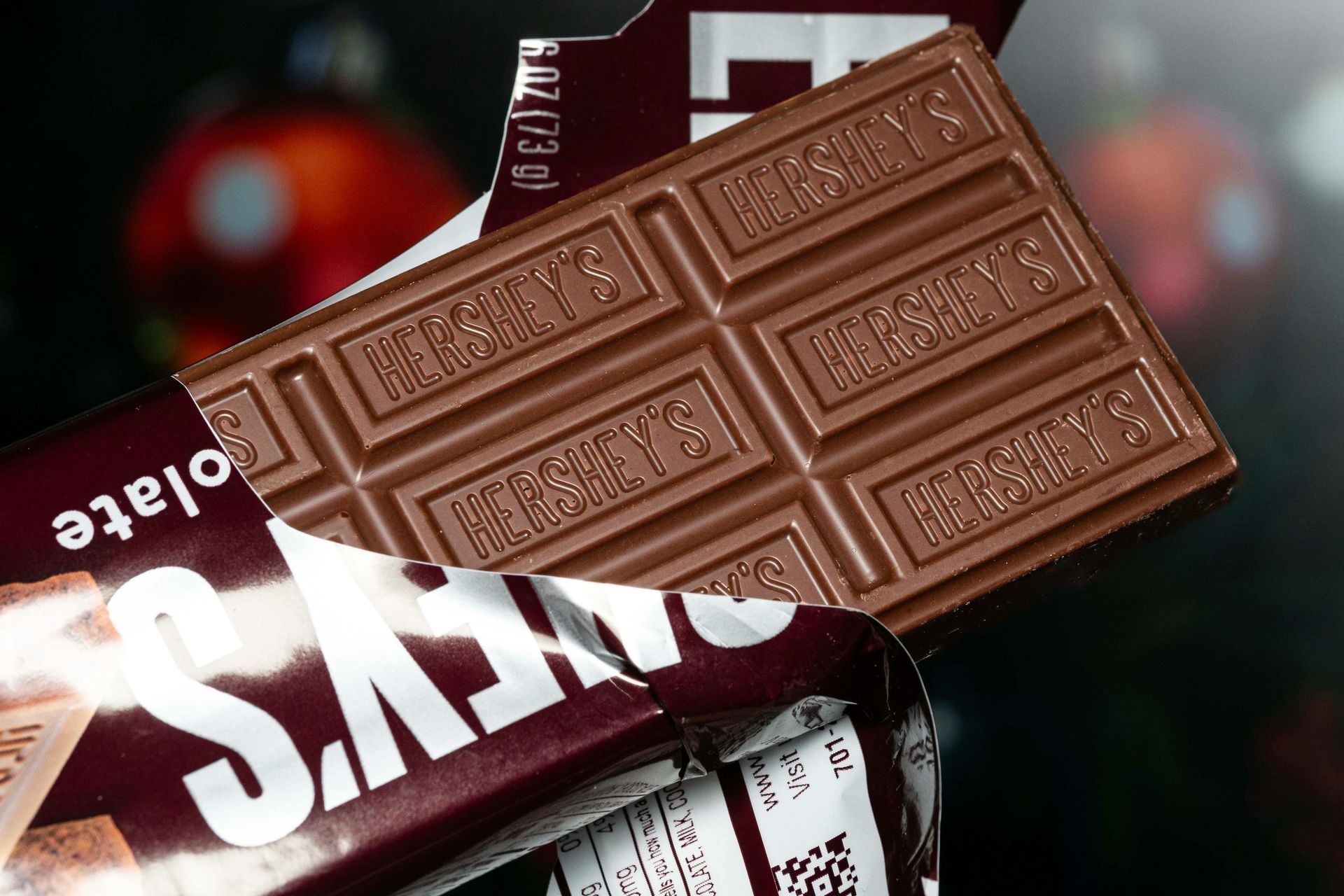 Hershey's chocolate bar partially unwrapped, showing a segmented milk chocolate bar. Dark red and white packaging in view.