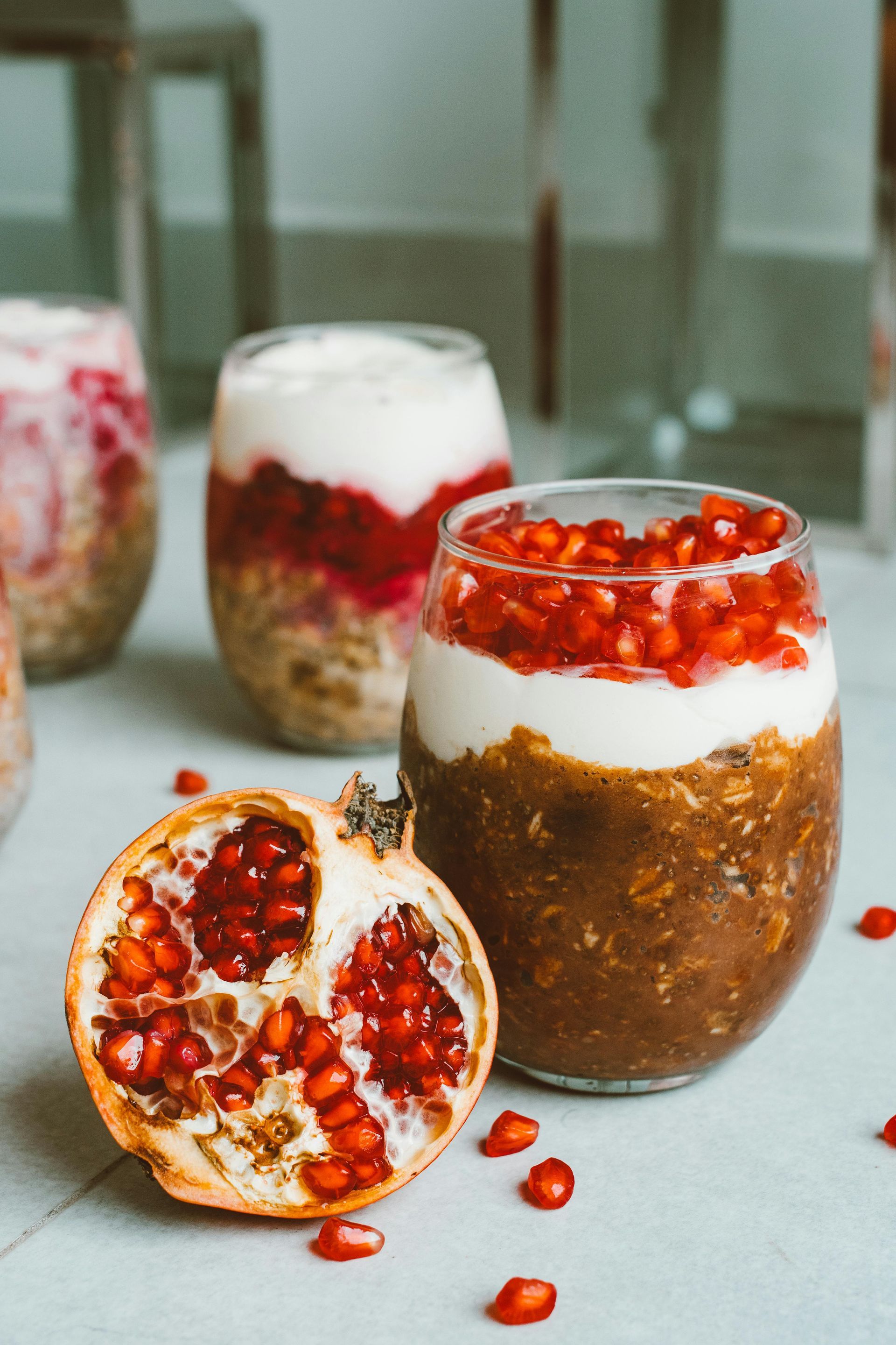 Pomegranate chia seed pudding layered with yogurt and pomegranate seeds in a glass. Half a pomegranate in foreground.