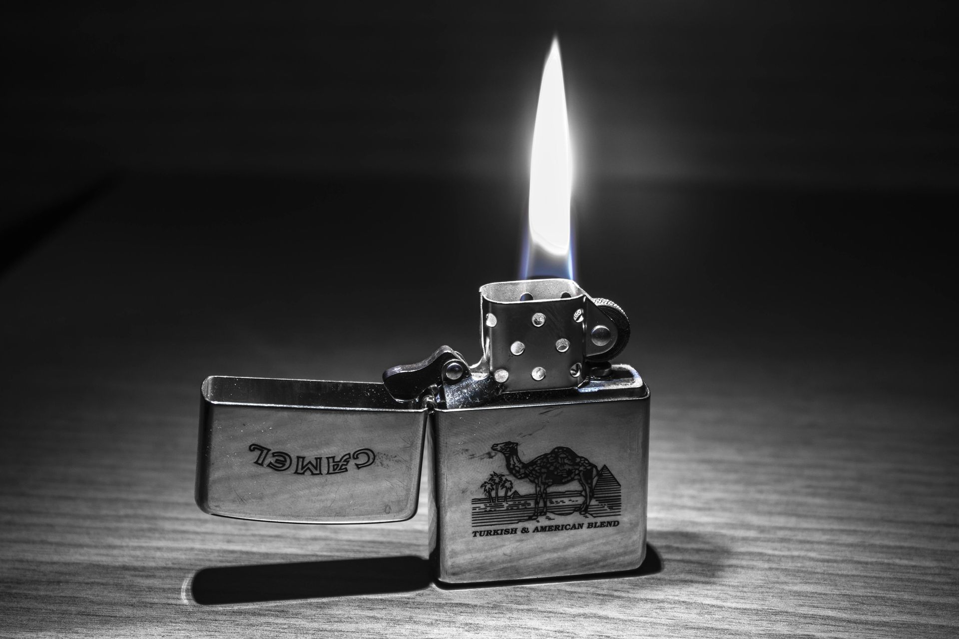 Camel lighter with flame lit, open on a wooden surface.