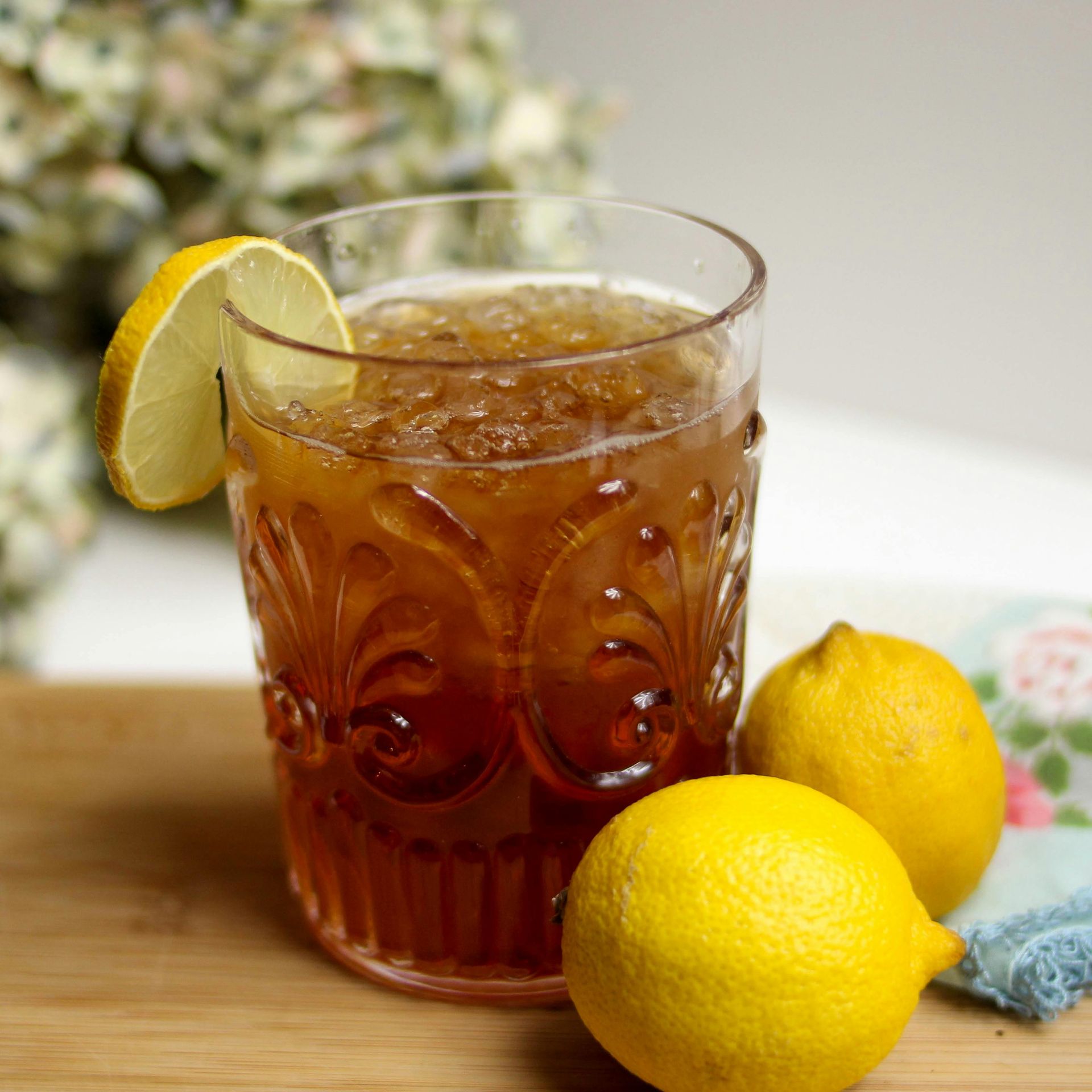 Glass of iced tea with lemon slice and two whole lemons.