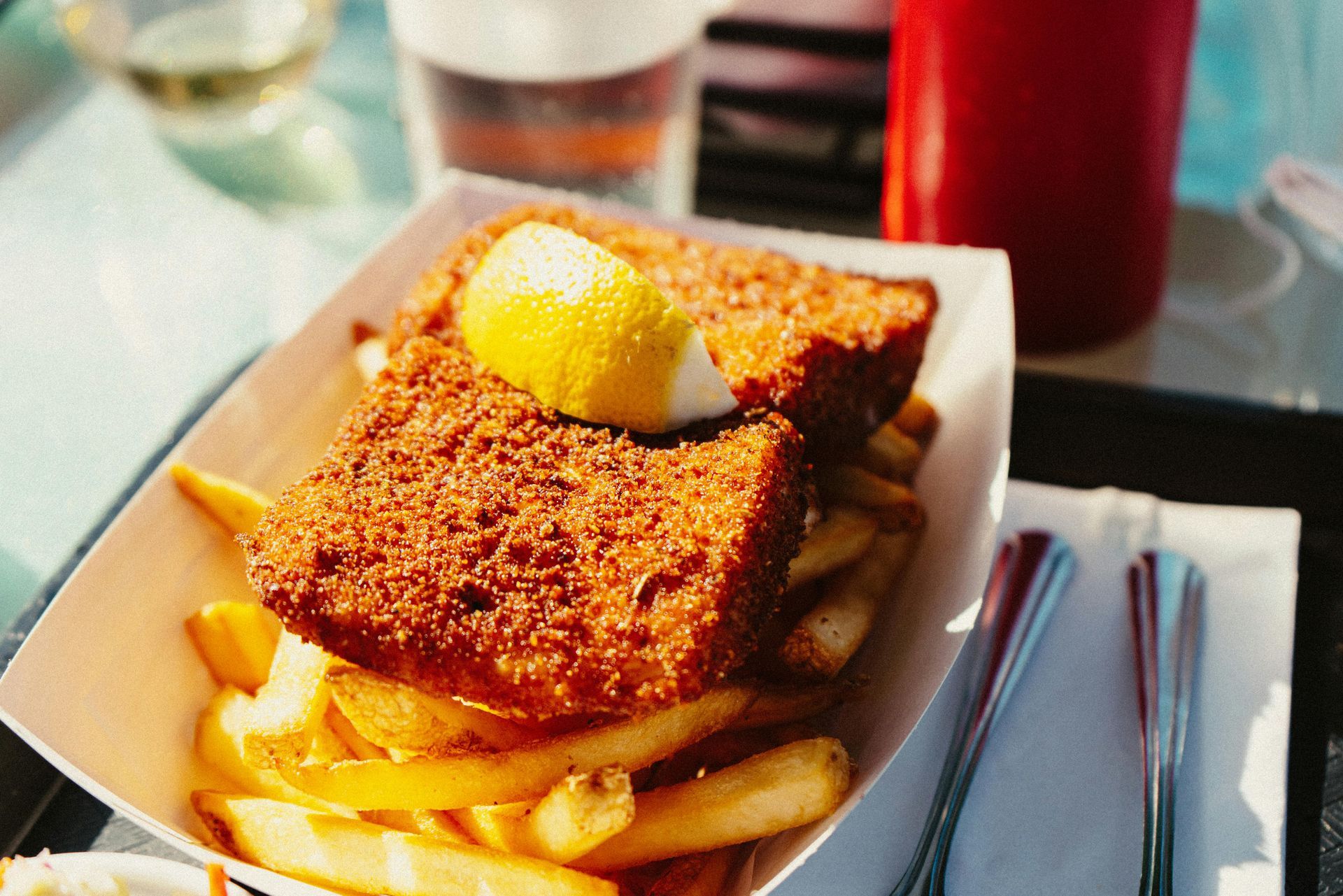 Fish and chips with lemon wedge on a paper tray, outdoor setting.