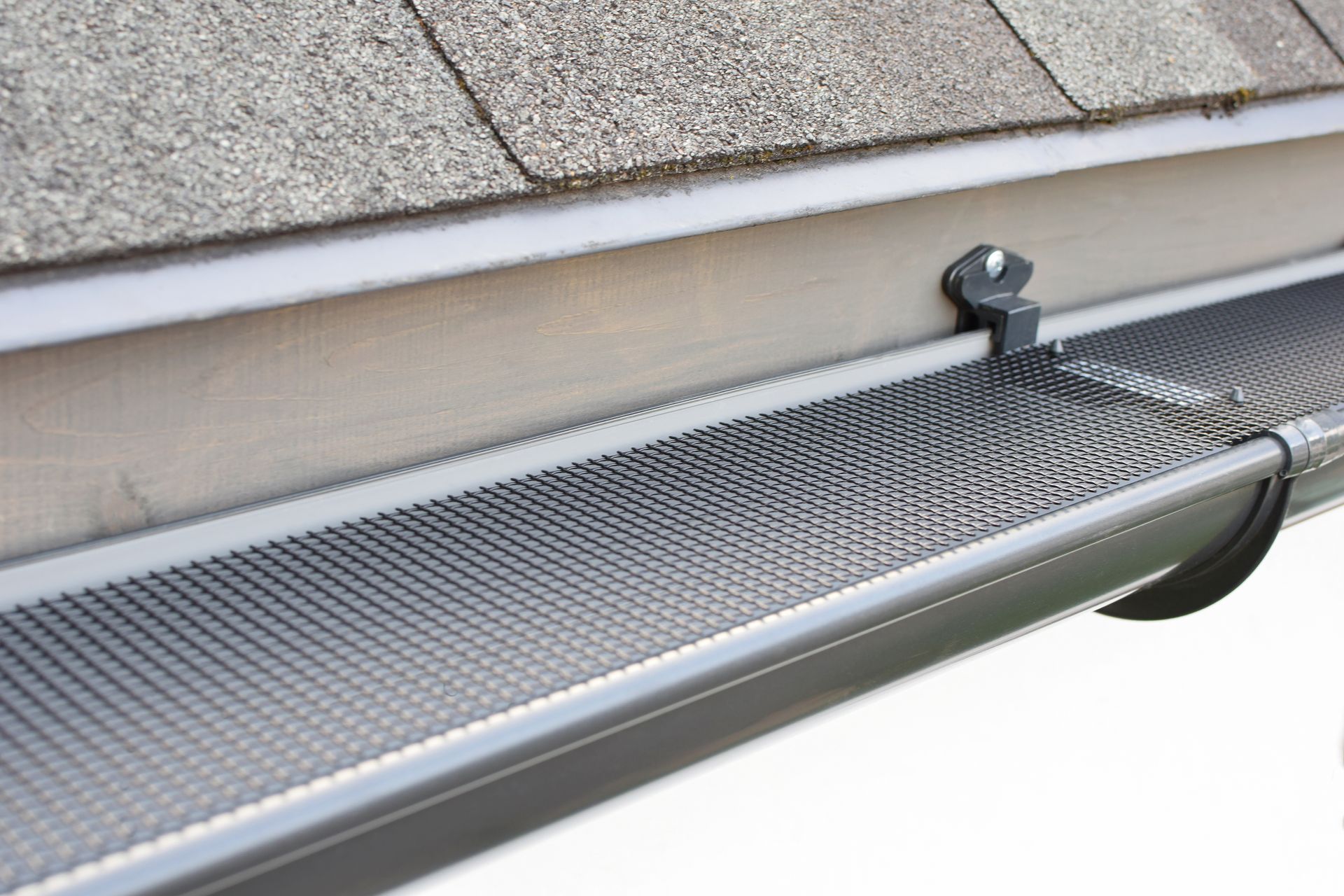 A close-up view of a black metal gutter guard installed over a grey seamless gutter attached to a roof eave.