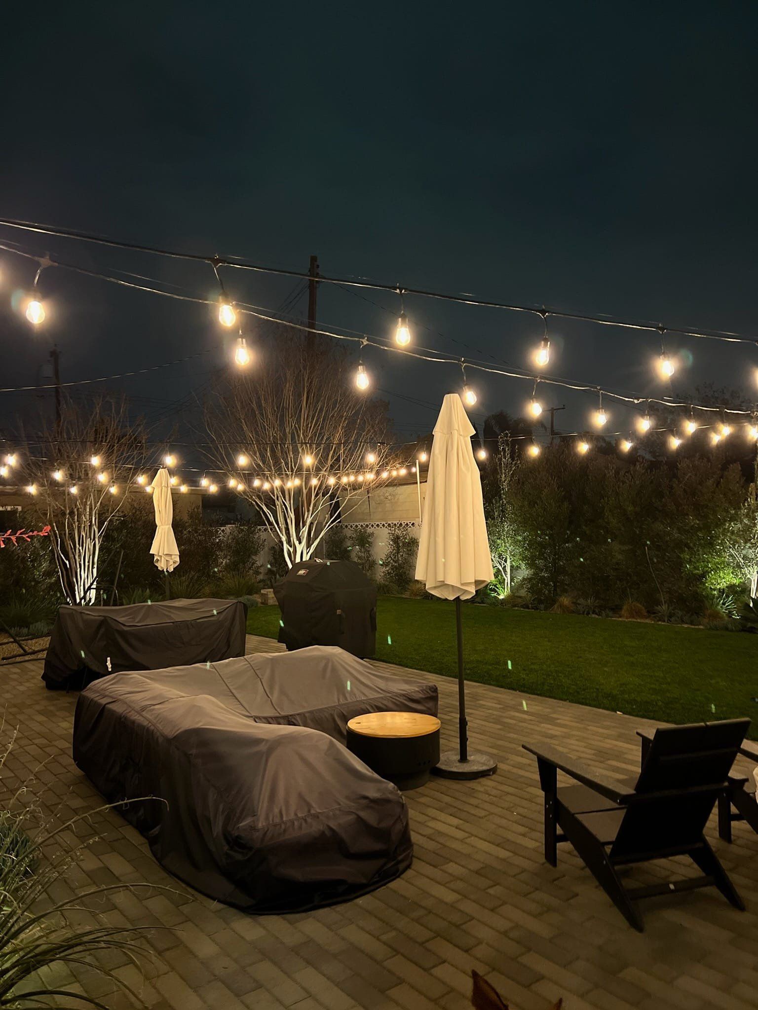A patio with a lot of furniture and umbrellas at night.