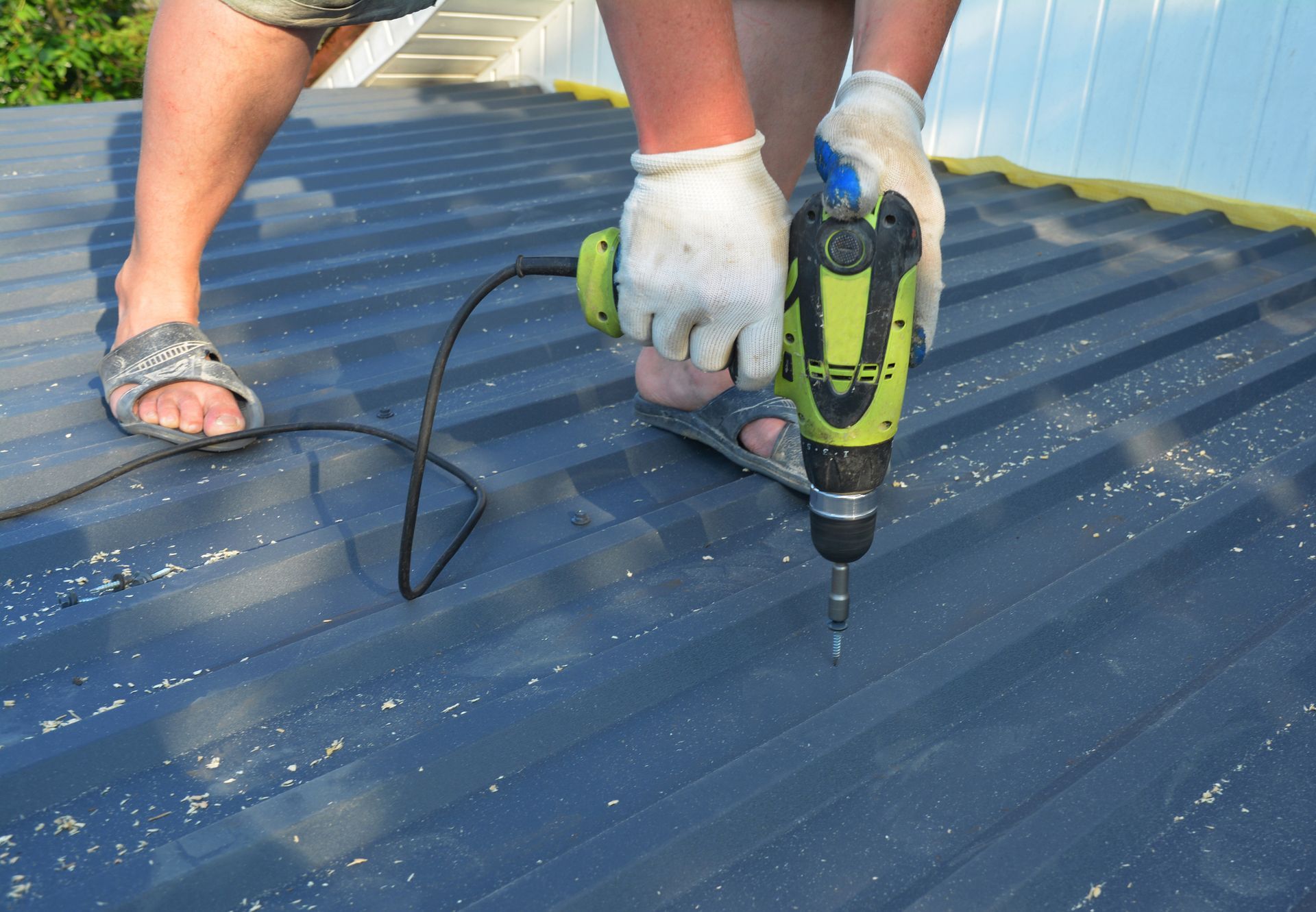 Residential roofer in Pensacola, FL installing metal roof tiles driving screws with a screwdriver.