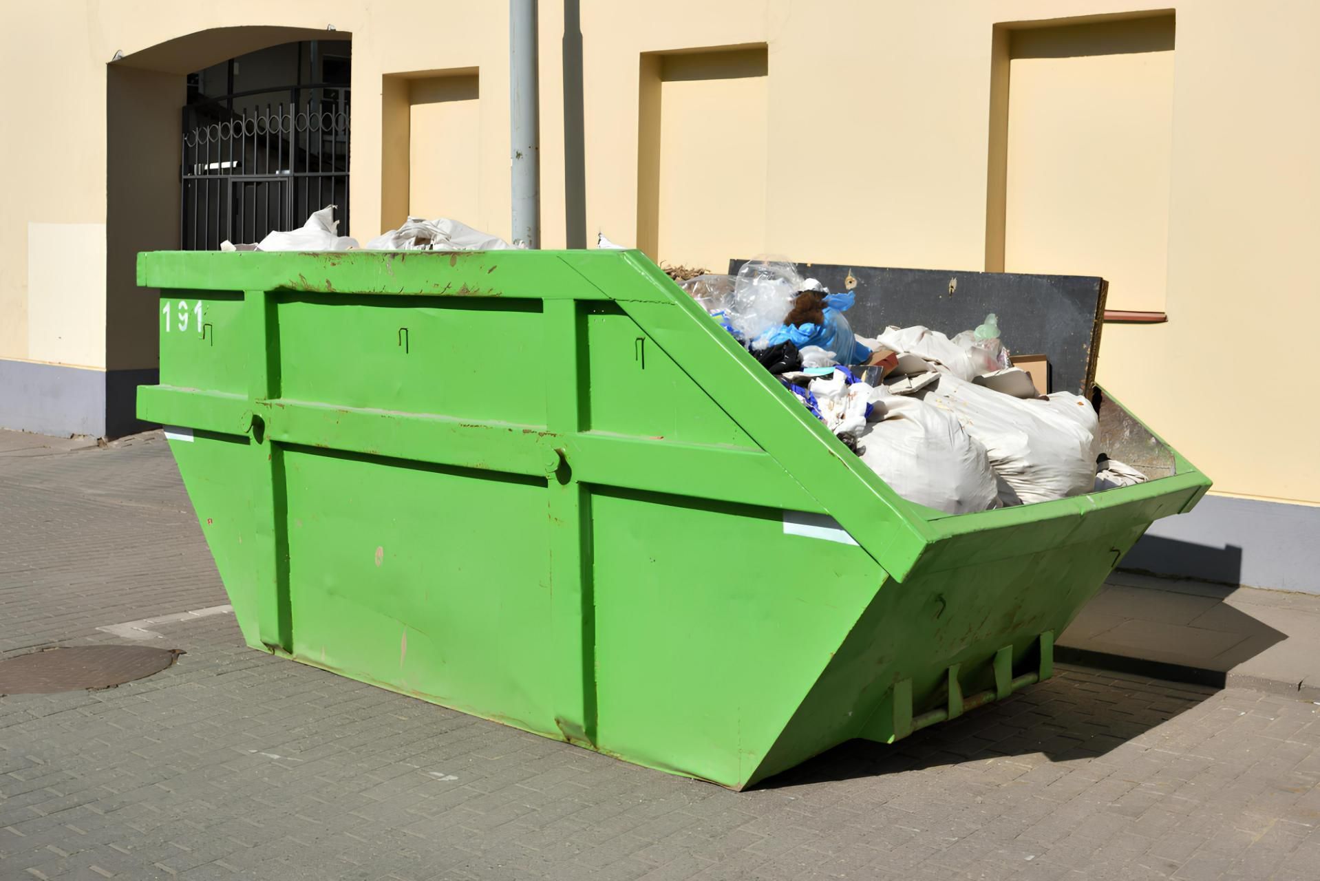 A Green Dumpster Filled With Trash is Parked in Front of a Building — IBS Skip Bins in Mapleton, QLD