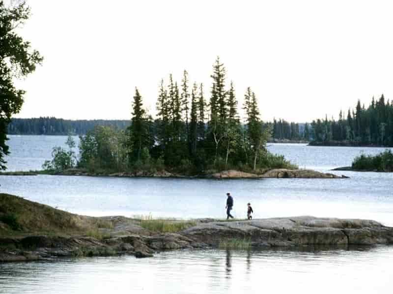 two people are walking on a rocky shore of a lake .