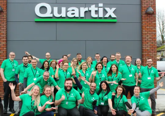 A large group of people are posing for a picture in front of a quartix store.