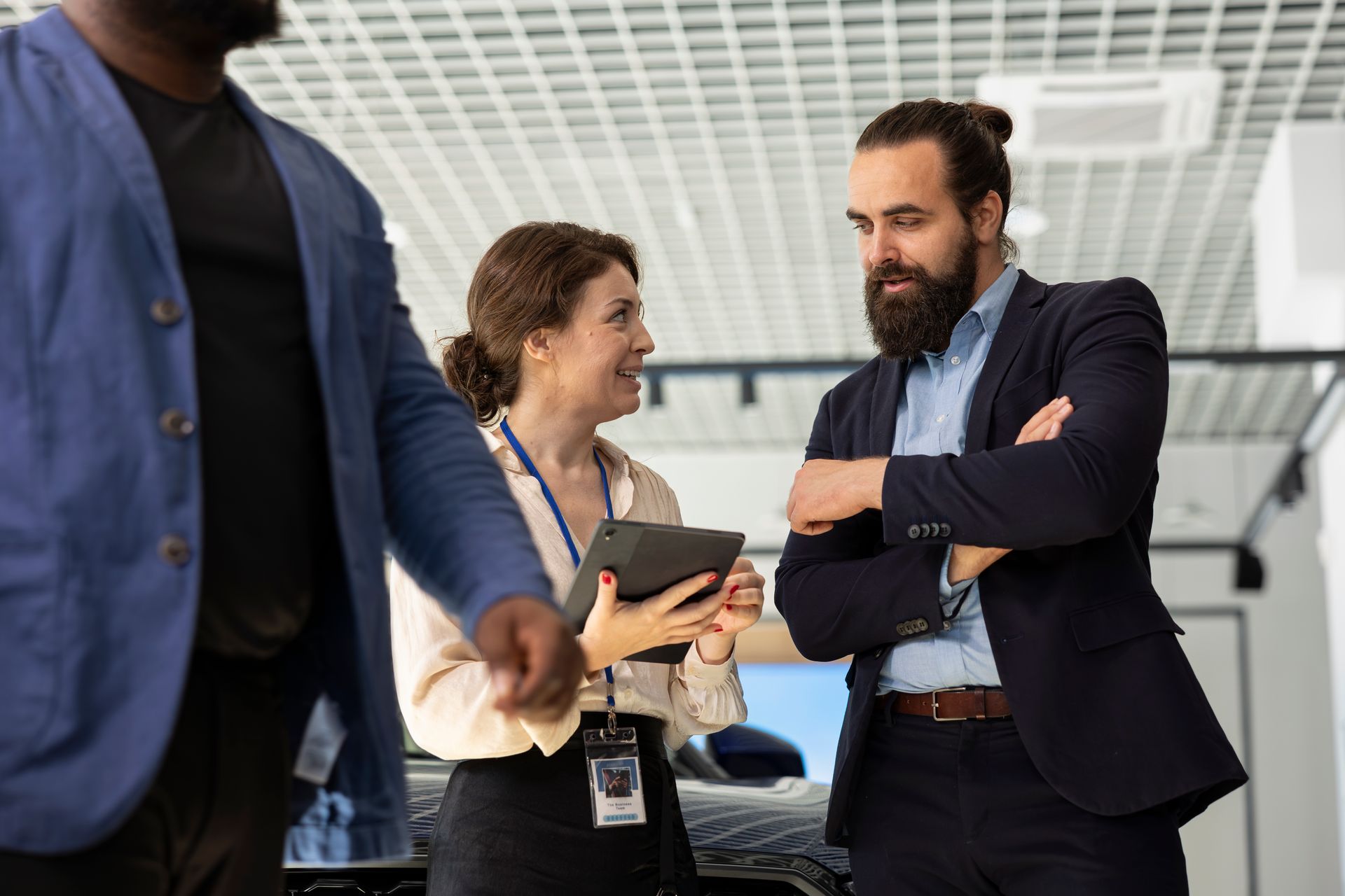 Salesperson showing a tablet to a man in a suit, another man stands nearby.