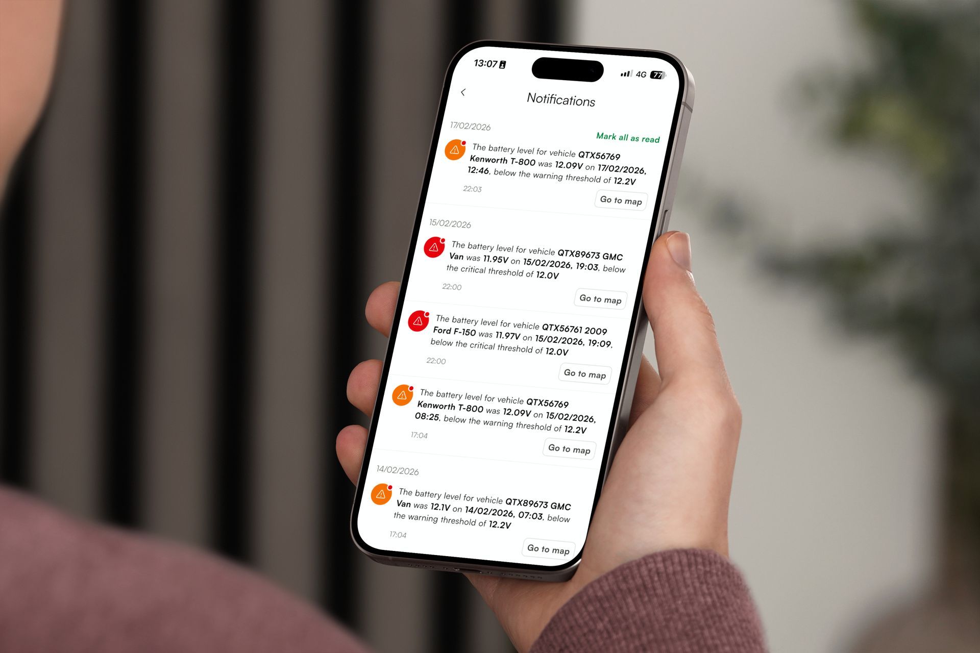 A person is holding a cell phone in front of a laptop.