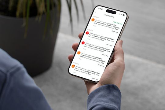 A person is holding a cell phone in front of a laptop.