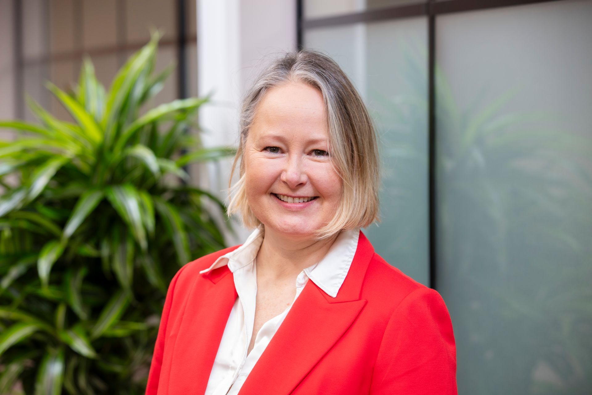 A woman in a red jacket and white shirt is smiling for the camera.