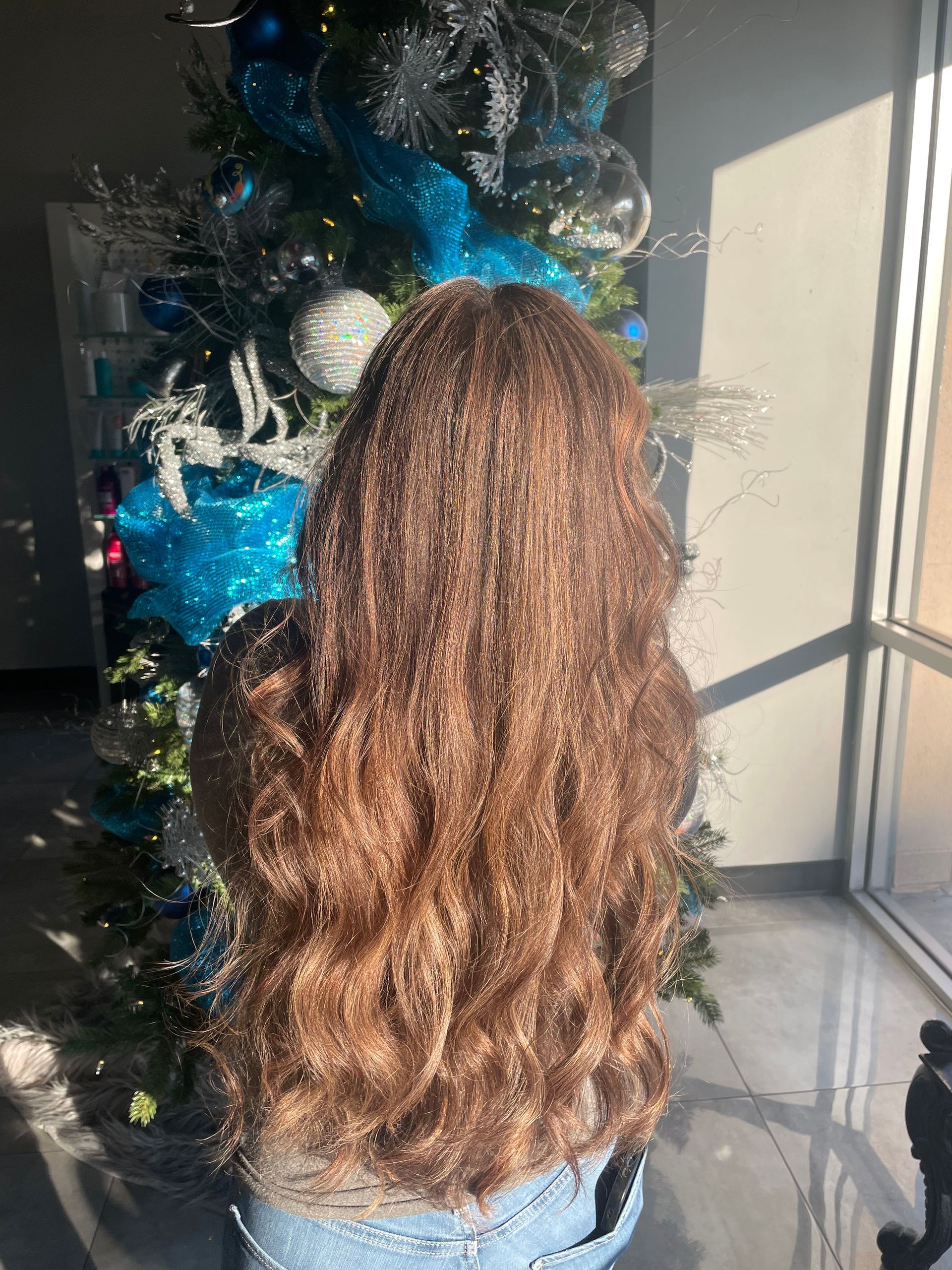 A woman with long hair is standing in front of a christmas tree.
