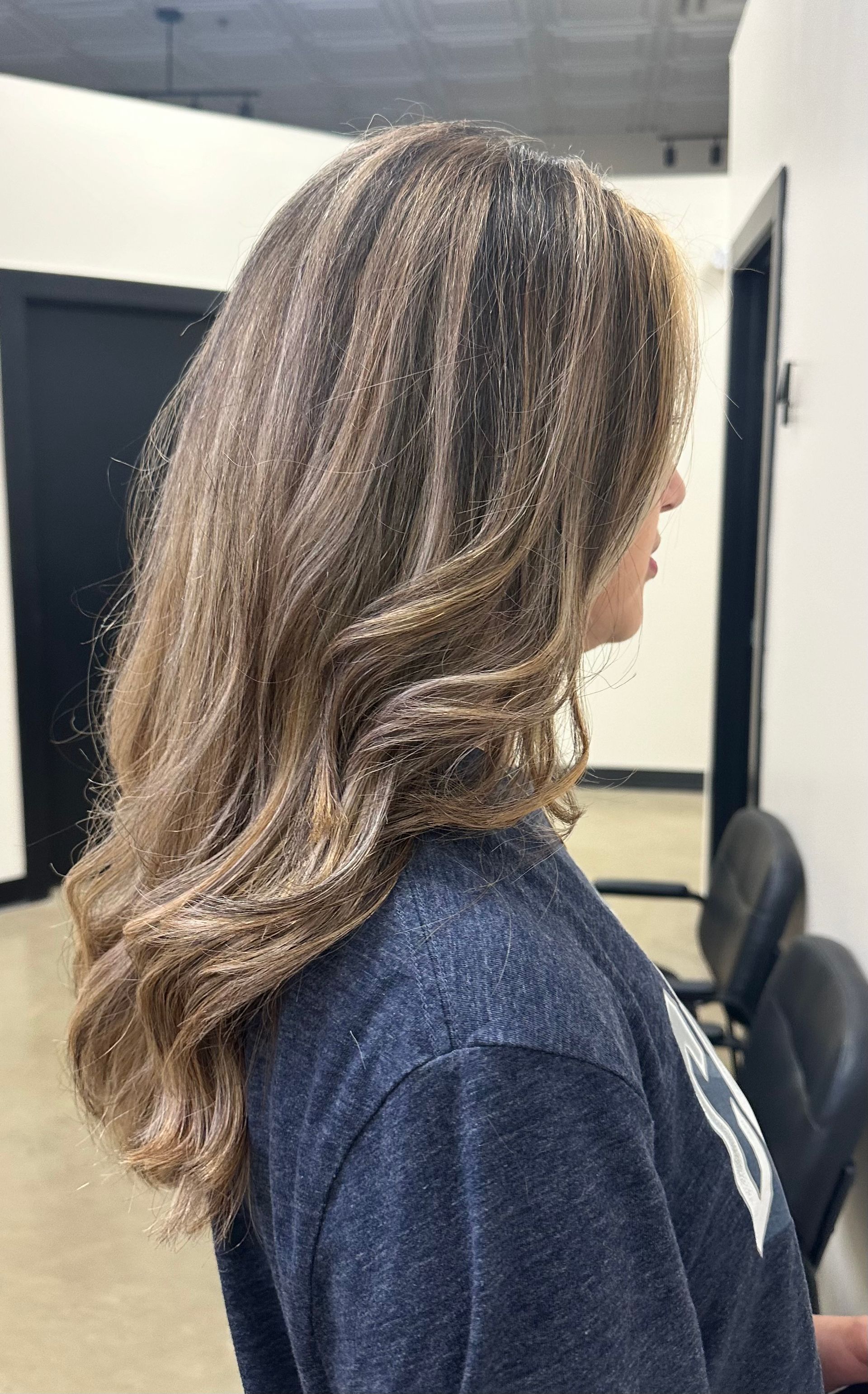 A woman with long brown hair is wearing a blue shirt and standing in a room.
