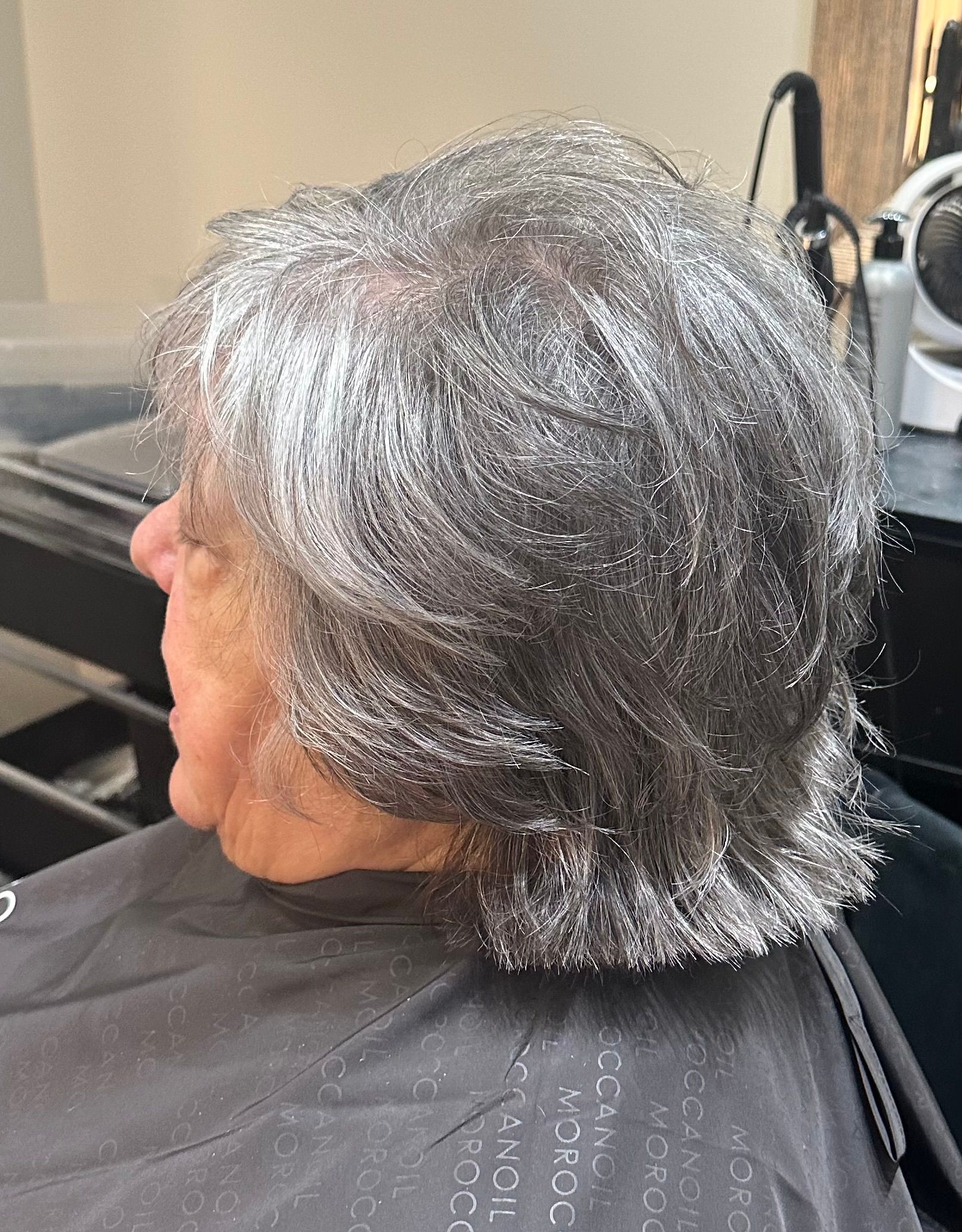 A woman with gray hair is sitting in a chair at a hair salon.