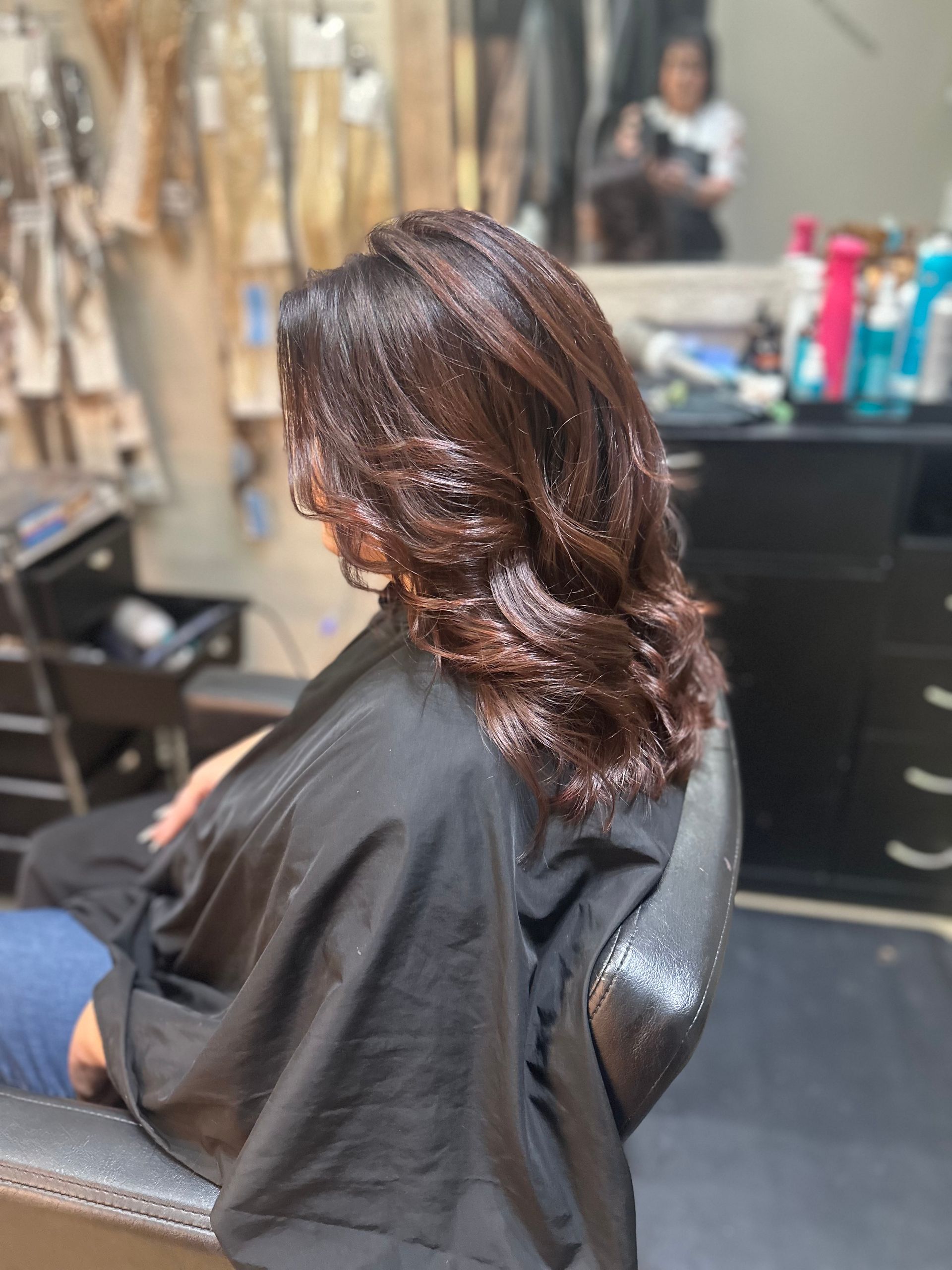 A woman is sitting in a chair in a salon getting her hair cut.