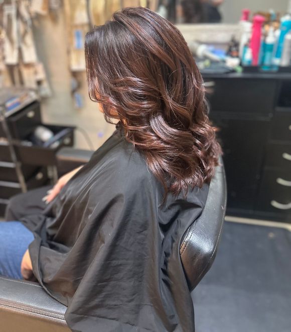 A woman is sitting in a chair in a salon getting her hair cut.