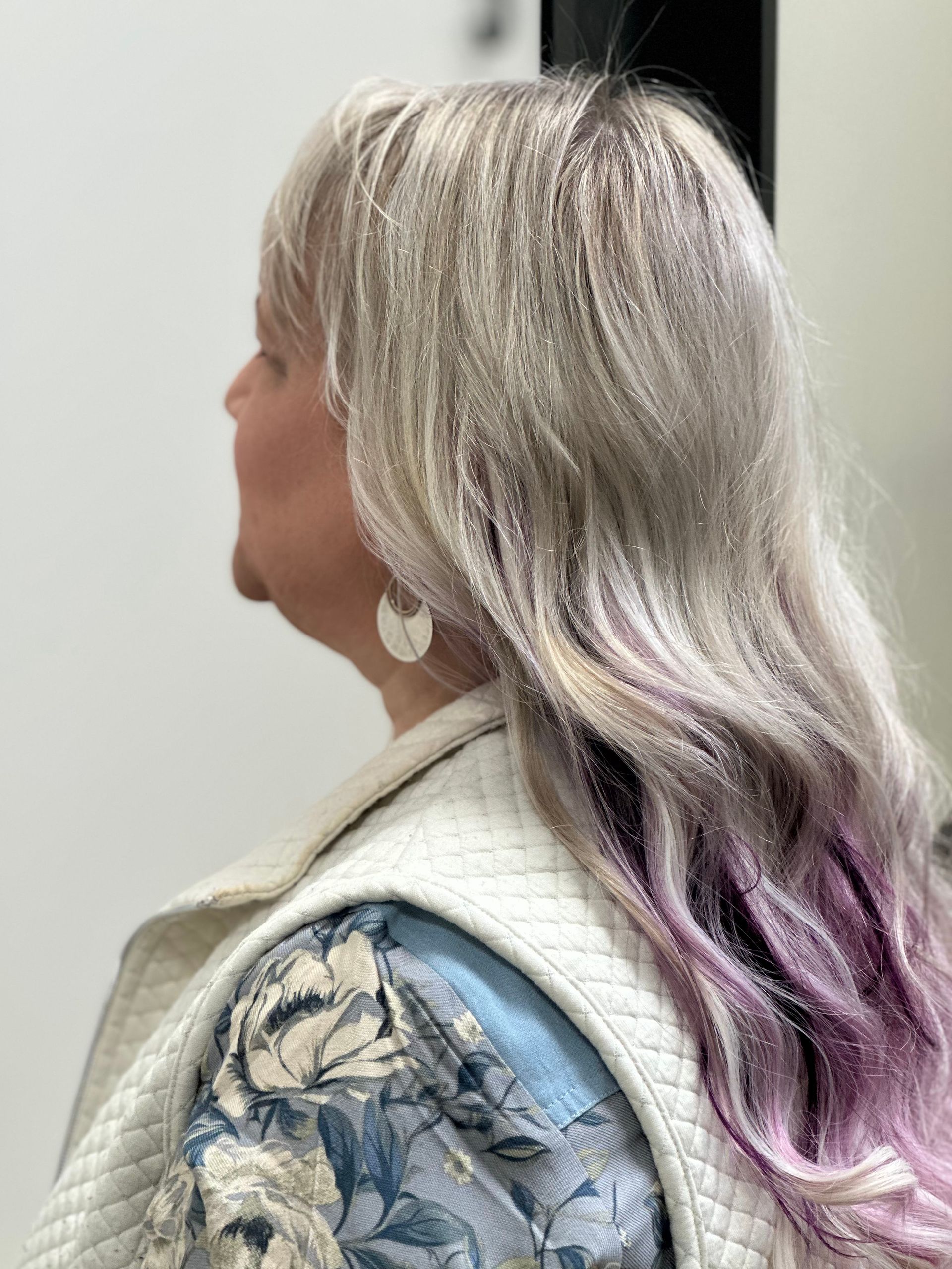 A woman with blonde and purple hair is wearing a floral shirt and a white vest.