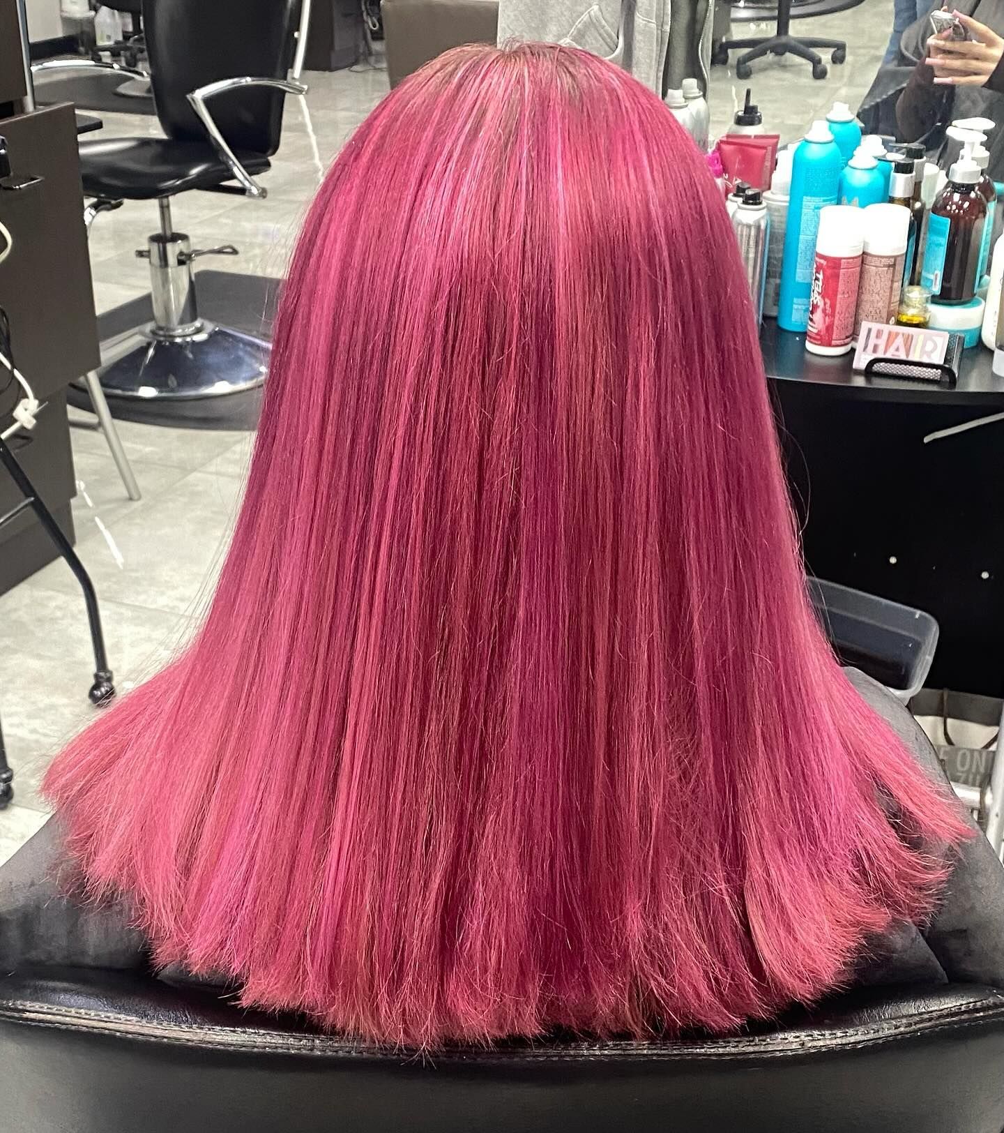 A woman with pink hair is sitting in a chair in a salon.