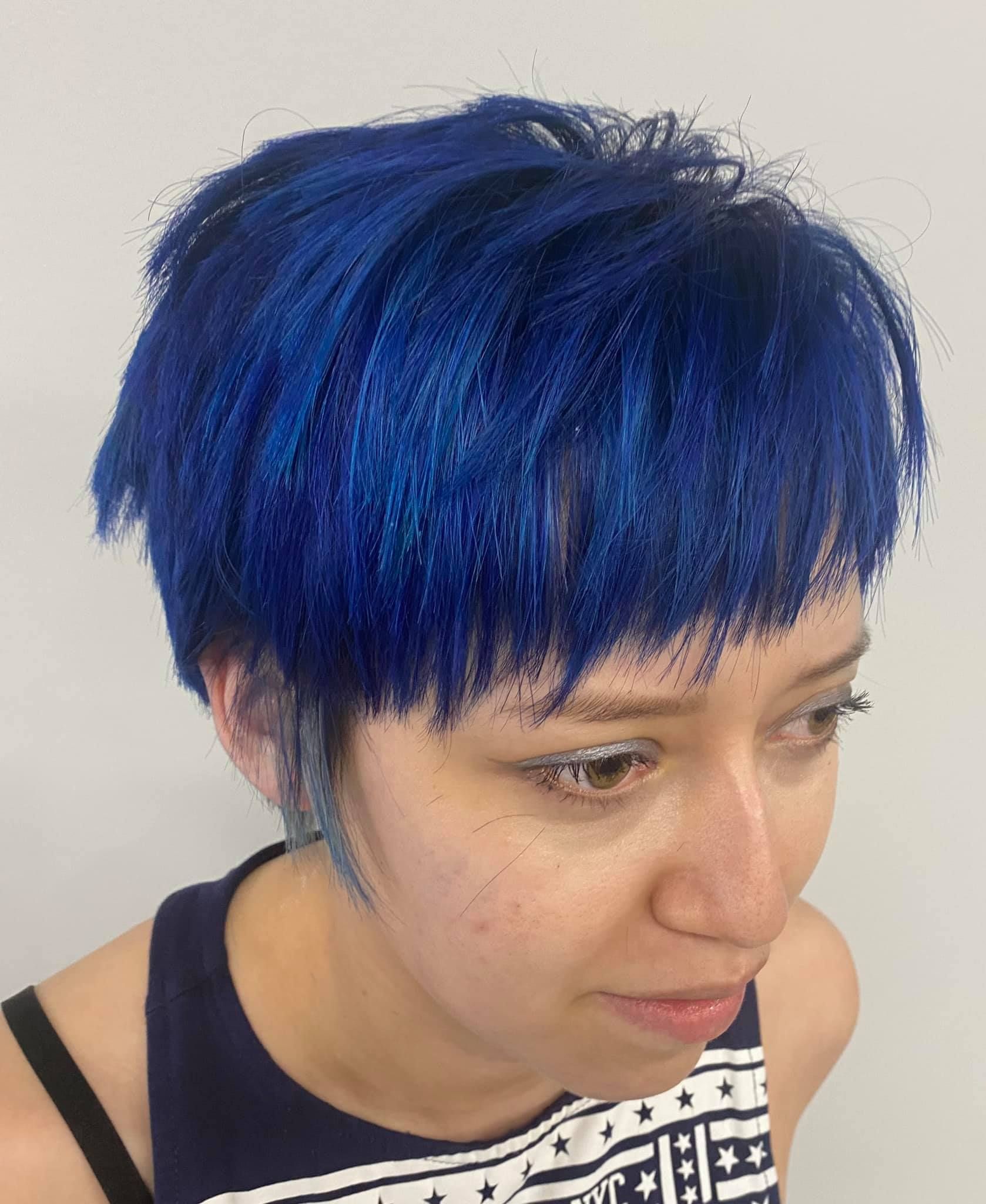 A woman with short blue hair is wearing a black tank top.