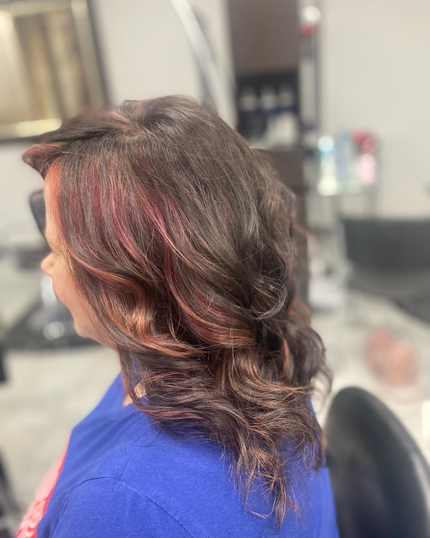 A woman in a blue shirt is getting her hair done in a salon.
