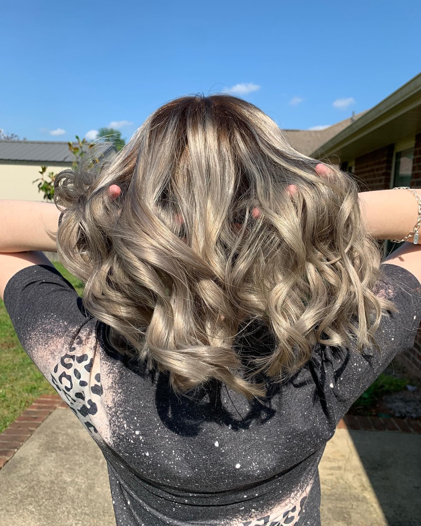 A woman is standing on a sidewalk with her hands in her hair.