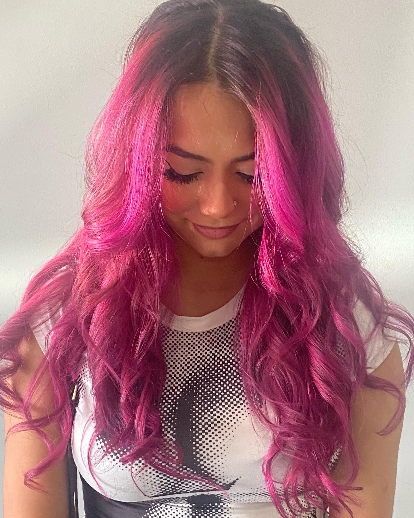 A woman with long pink hair is wearing a white shirt