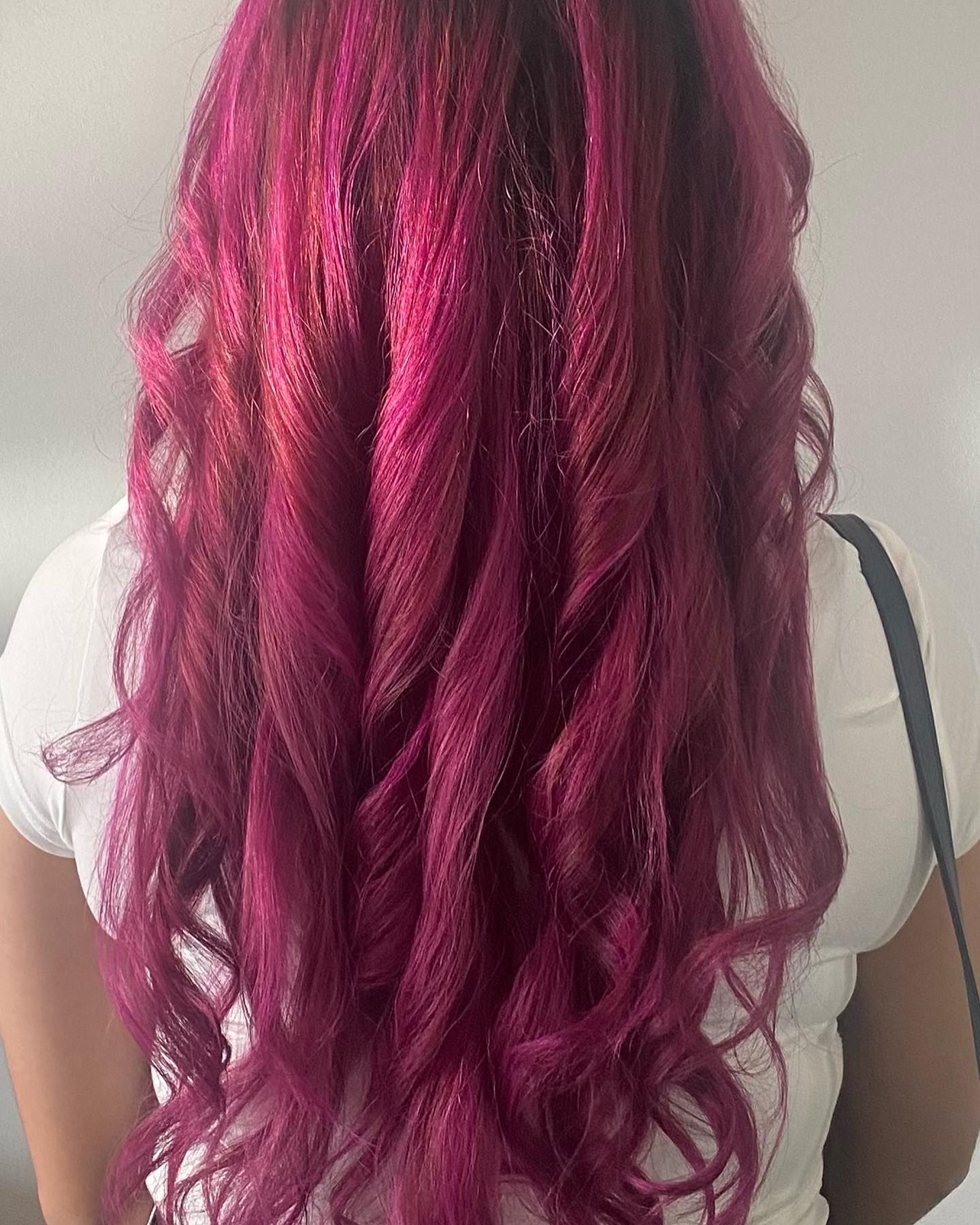 A woman with long purple hair is wearing a white shirt.